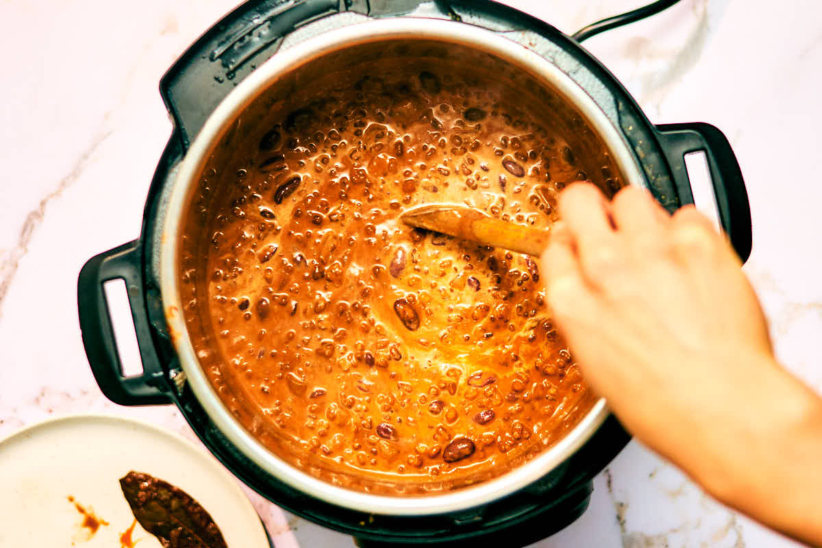 Kidney beans and cream being stirred into Dal Makhani in an Instant Pot.