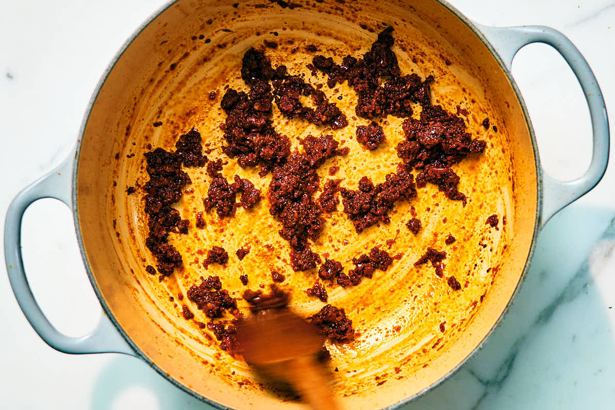 Thai red curry paste and spices being cooked in a pot with a wooden spoon.