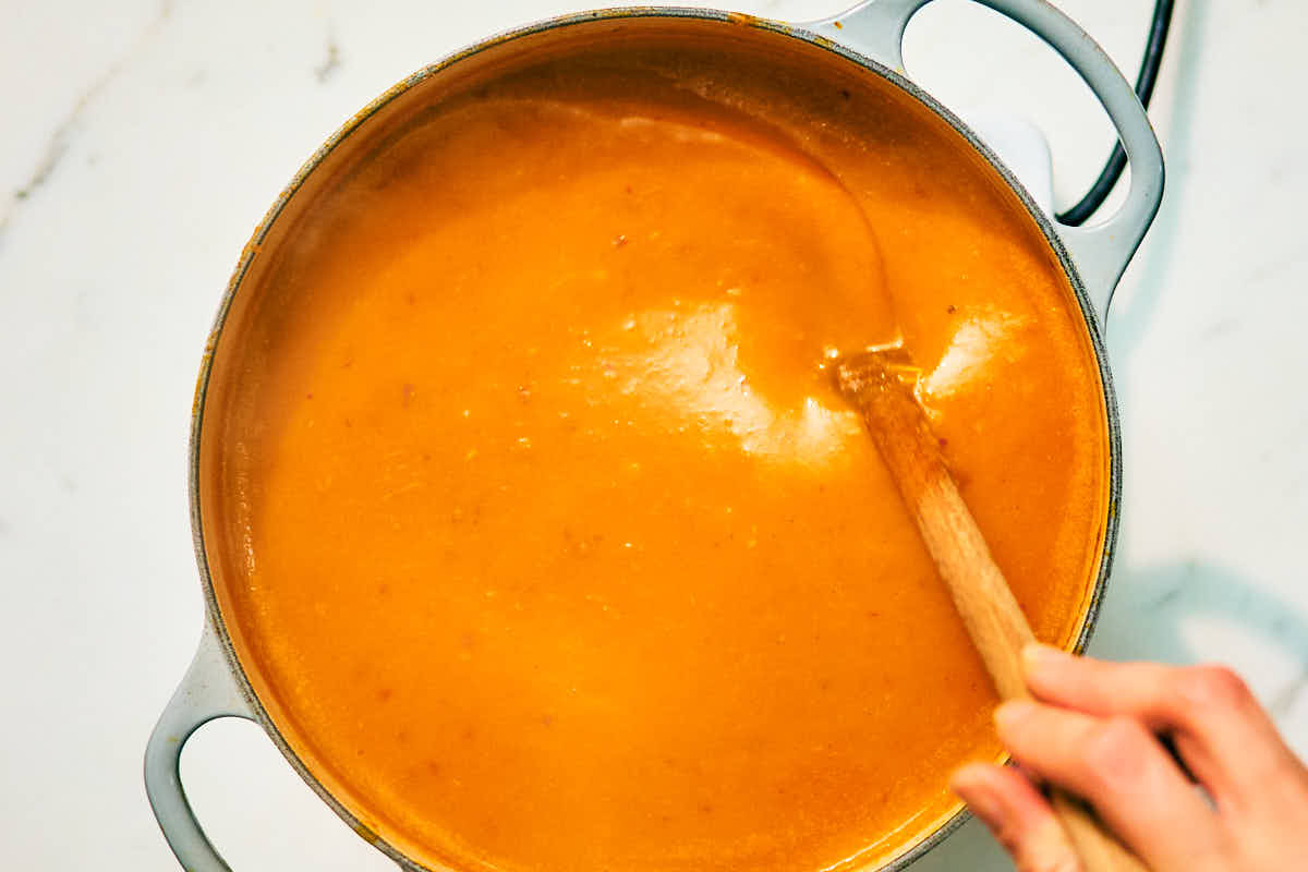 Creamy kabocha squash soup with coconut milk being stirred in a pot.
