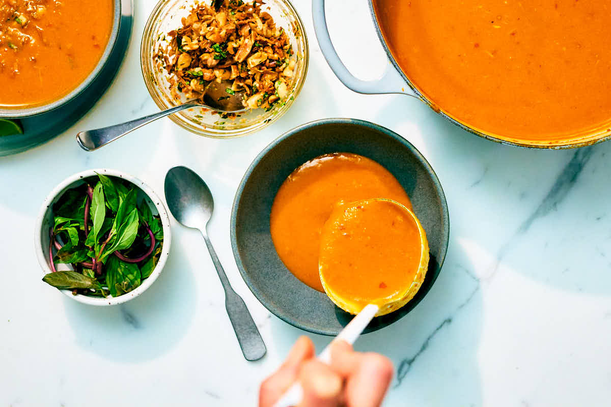 Kabocha Squash Soup being ladled into bowls on a marble counter.