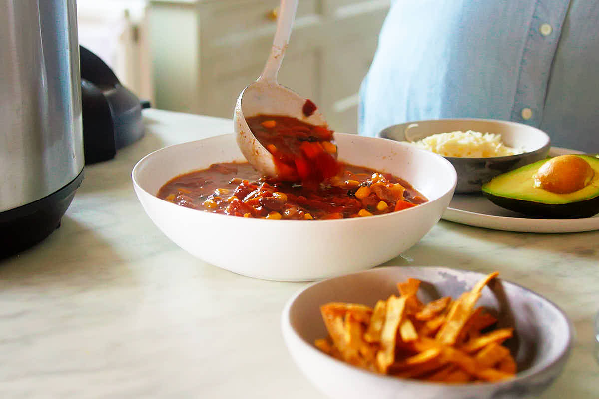 Instant Pot Vegetarian Chili being ladled into bowls with garnishes.