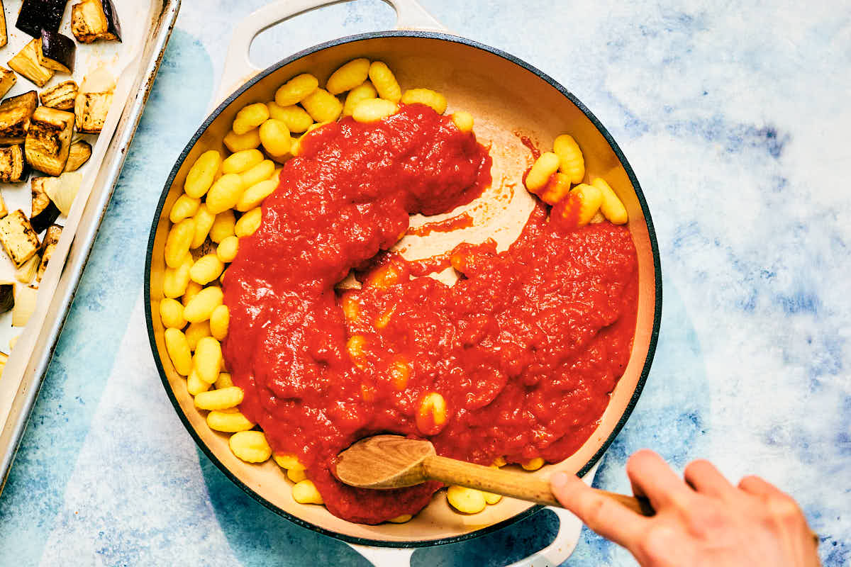 Baked gnocchi being combined with marinara sauce in a skillet.