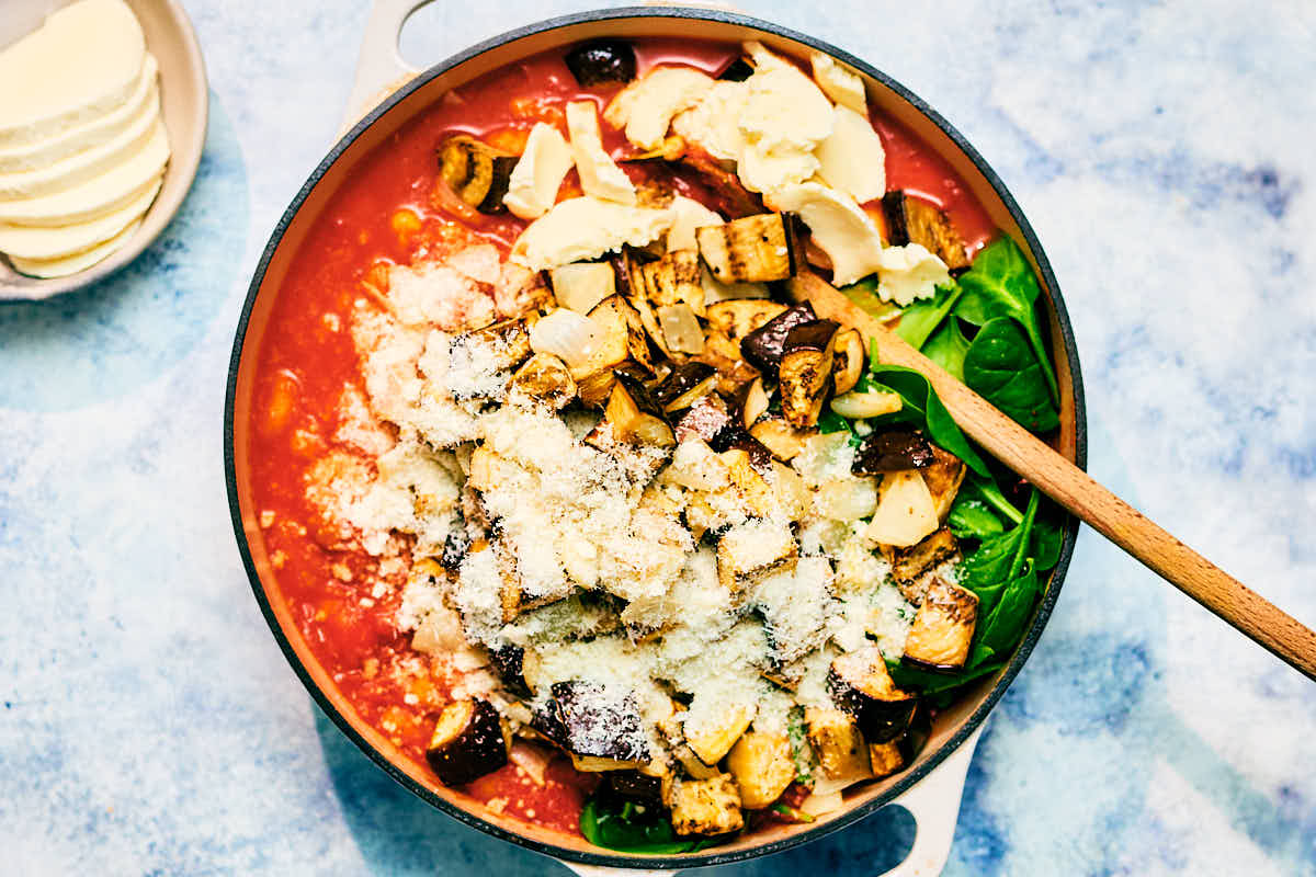Stirring together roasted eggplant, onion, spinach, cheese, with gnocchi and tomato sauce.