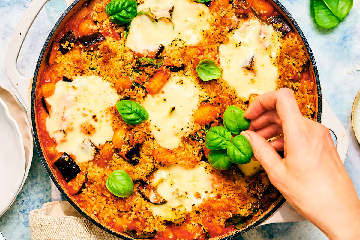 Crispy Eggplant Parmesan Tomato Gnocchi Bake being garnished with basil.