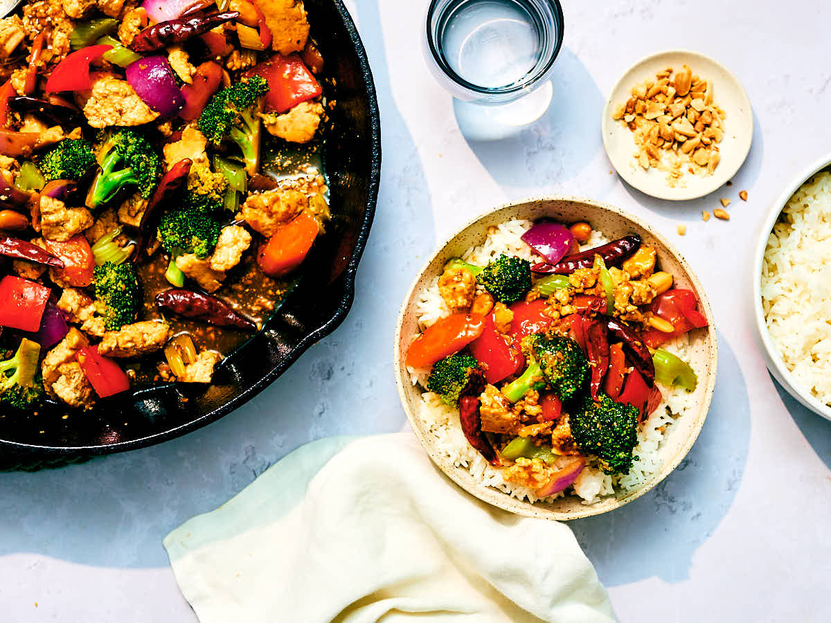 Kung Pao Vegetables, Tofu, and peanuts in a skillet and bowl on a dinner table.