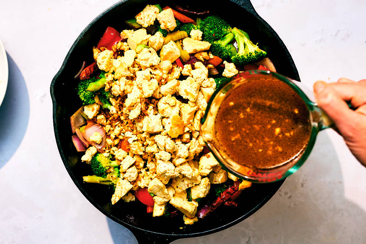 Sauce being poured on top of Kung Pao Vegetables with Tofu in a skillet.