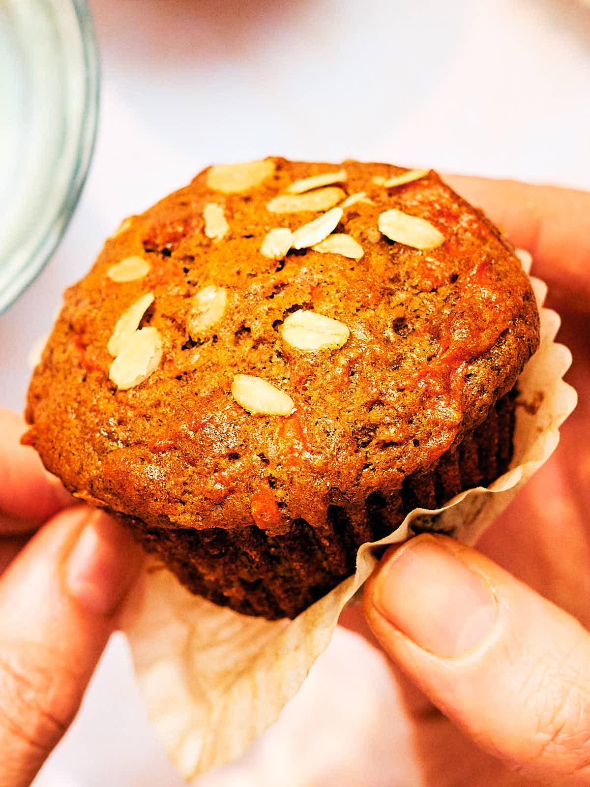 A woman's hand holding a moist, vegan Banana Carrot Muffin.