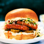 Nashville Hot Tofu Sandwich on a plate with slaw, pickles, brioche bun.