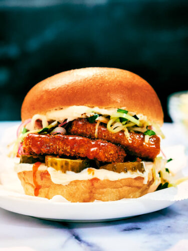 Nashville Hot Tofu Sandwich on a plate with slaw, pickles, brioche bun.