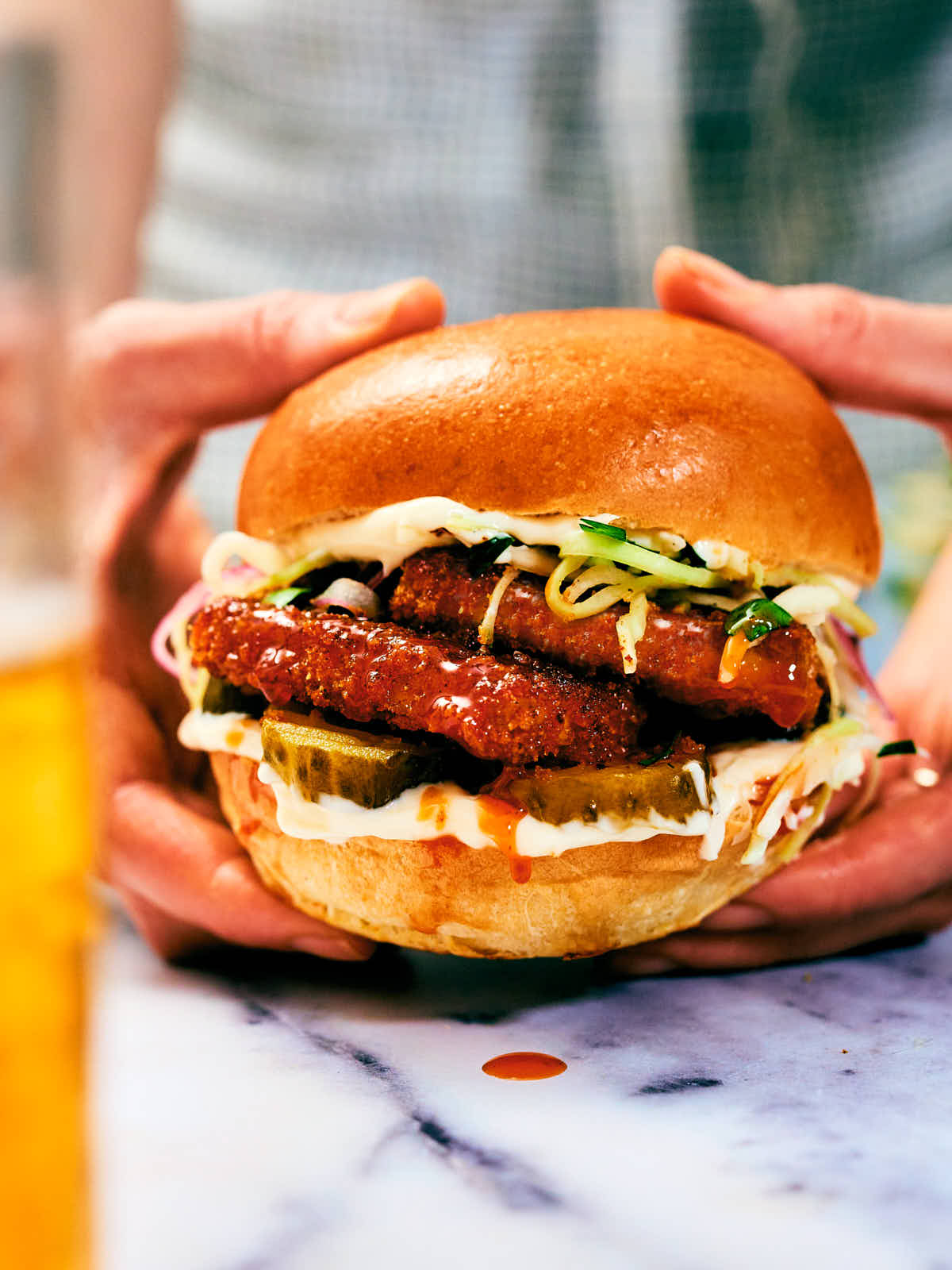 Hands holding a Nashville Hot Tofu Sandwich with coleslaw and pickles.