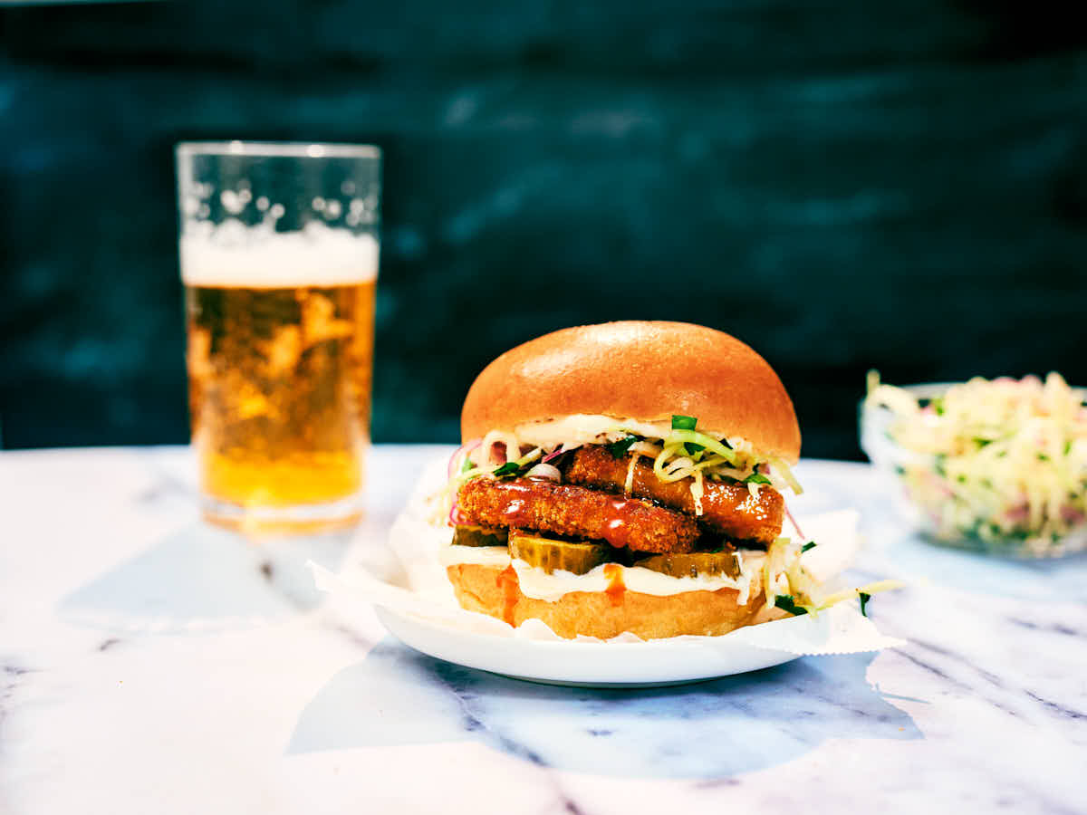 A Nashville-inspired Hot Tofu Sandwich, drink, and cabbage slaw on marble table.