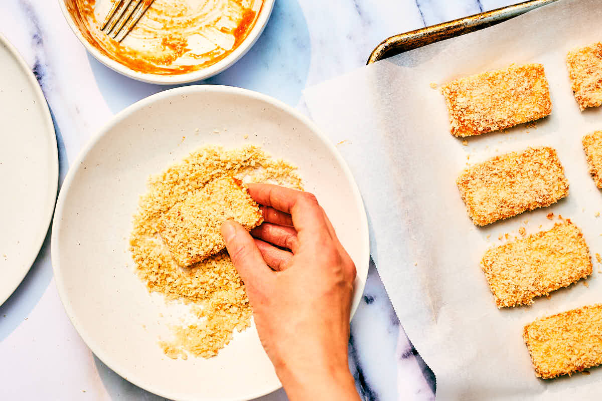Tofu slices being dipped in panko breadcrumbs.