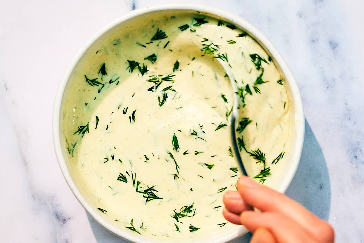 Dill Pickle Ranch Dressing with dill being mixed in a bowl.