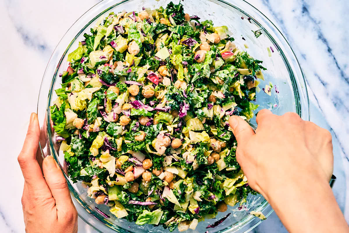 High protein Dill Pickle Salad being tossed with dressing in a bowl.