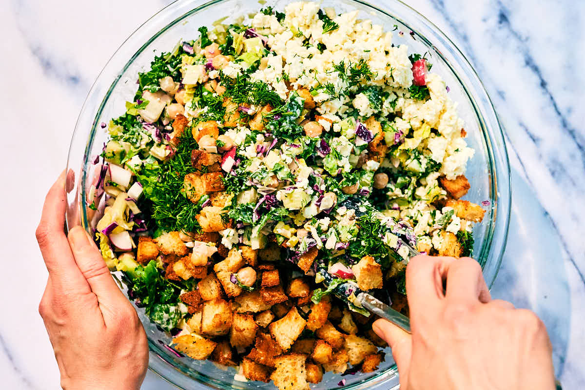 Croutons and feta being tossed into a kale dill pickle salad.