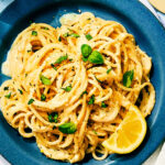 Lemon Pesto Pasta topped with basil on a plate with a slice of lemon.