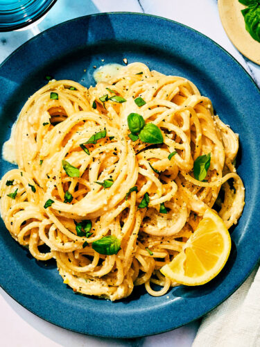 Lemon Pesto Pasta topped with basil on a plate with a slice of lemon.