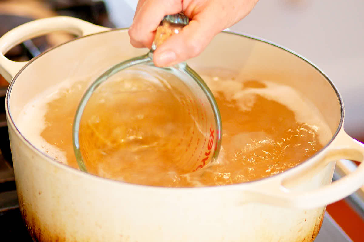 Pasta water being scooped out of a pot of boiling pasta.