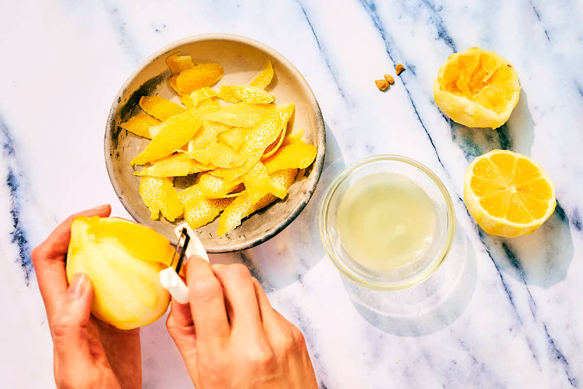 A vegetable peeler being used to remove lemon rind from fresh lemons.