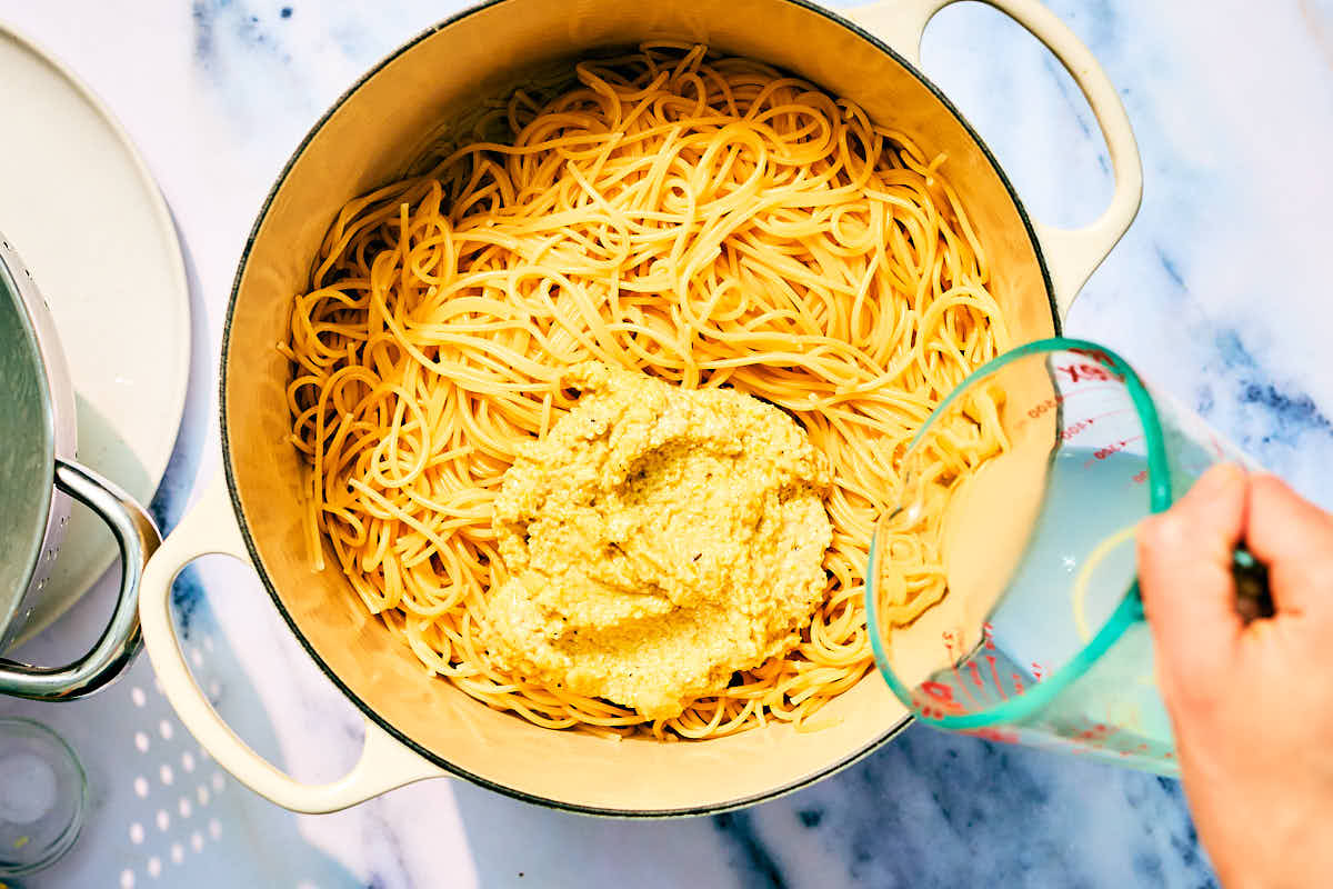 Cooked pasta in a pot with lemon pesto and pasta water being added.