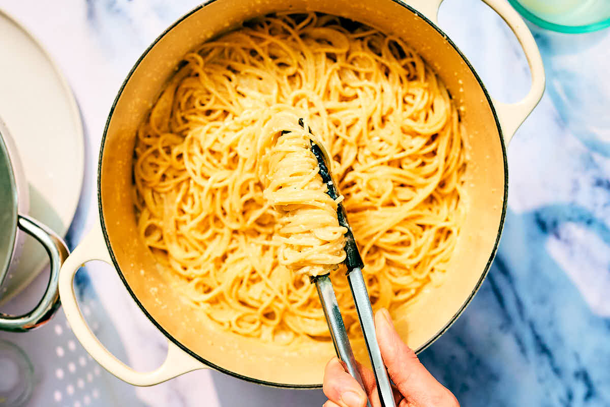 Tongs tossing spaghetti with lemon pesto until creamy.
