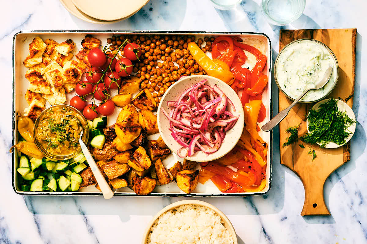 Baked feta, vegetables, roasted chickpeas, and potatoes on a sheet pan with tzatziki.