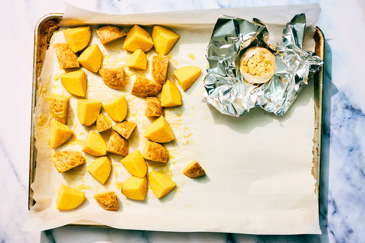 Potatoes and garlic on a baking sheet for roasting.