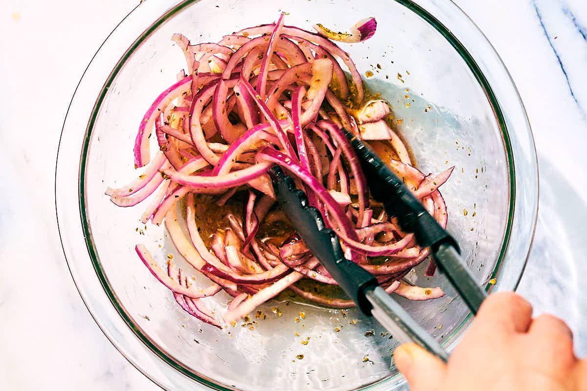 Marinated red onions being tossed in a bowl.