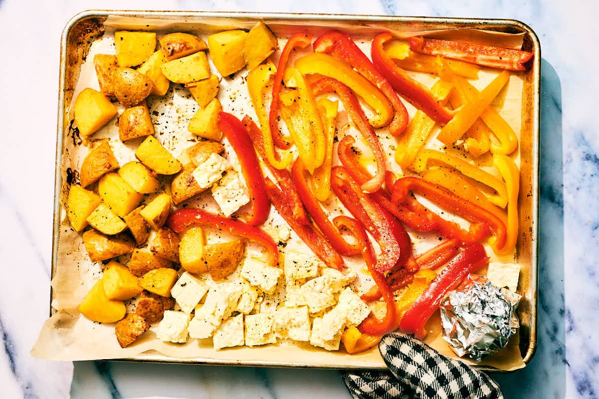 Feta, bell peppers, potatoes on a baking sheet to be roasted.