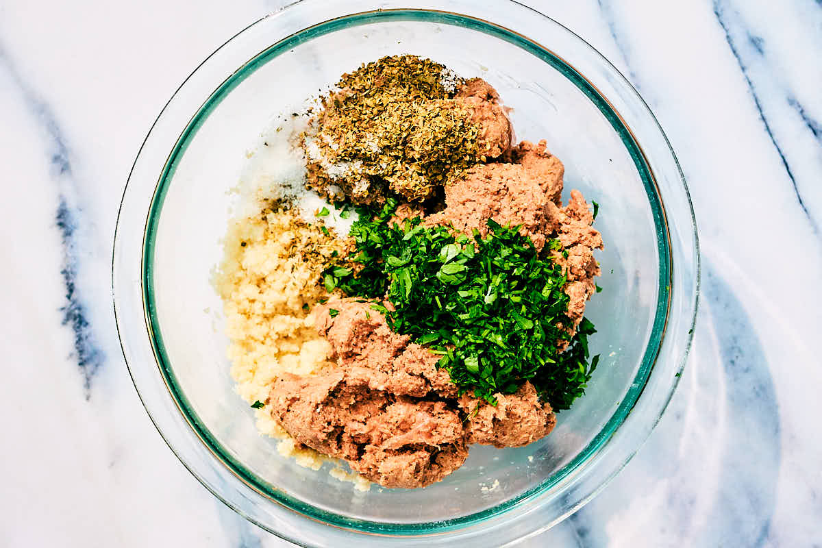 Plant based sausage in a bowl with breadcrumnbs, parsley, and herbs for vegan meatballs.