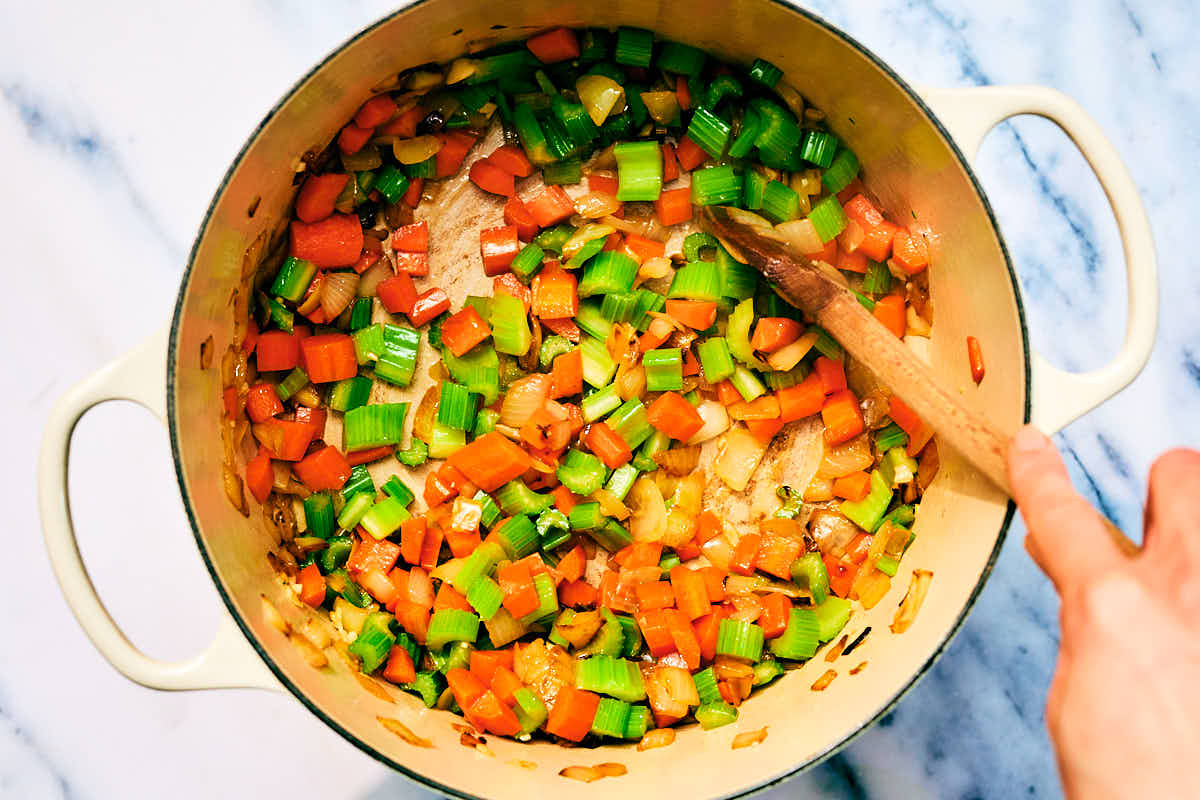 Onion, carrots, celery, and garlic being sauteed in a pot for soup.