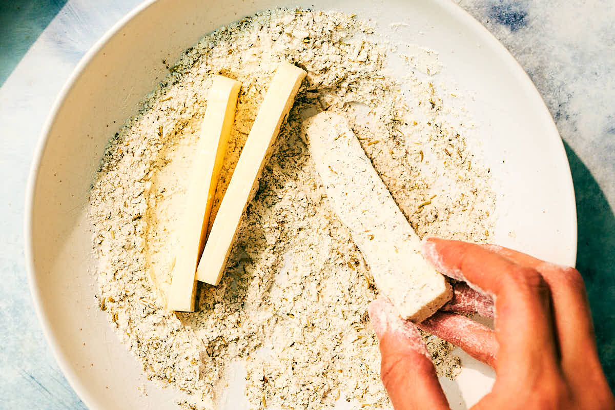 Halloumi being tossed in a bowl of flour, Italian seasoning, and spices.