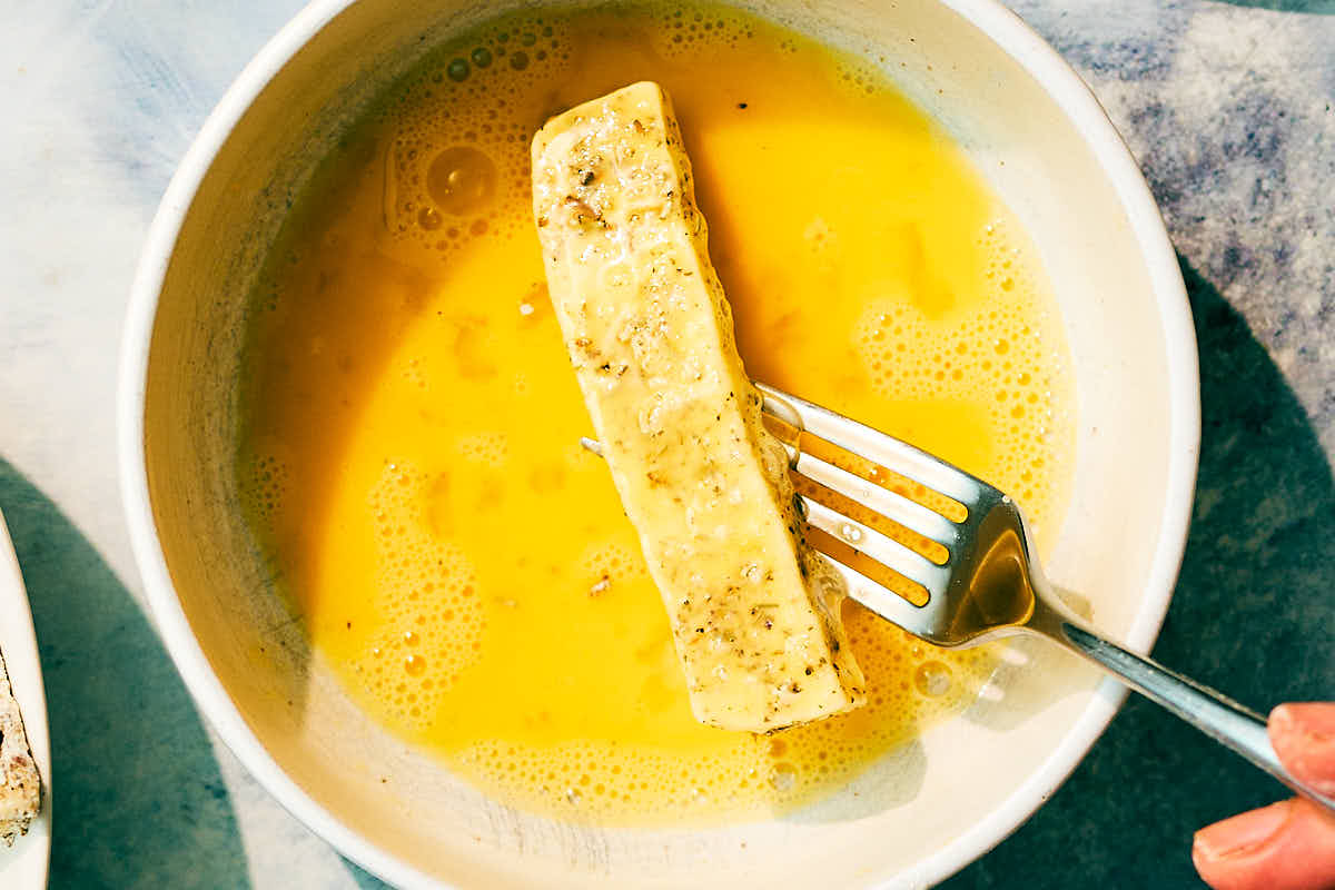 Flour dredged halloumi being dipped in a bowl of whisked egg.