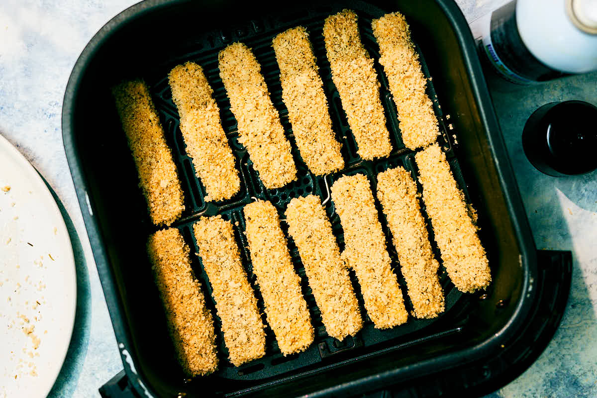 Panko crusted halloumi fries in an air fryer basket before baking.