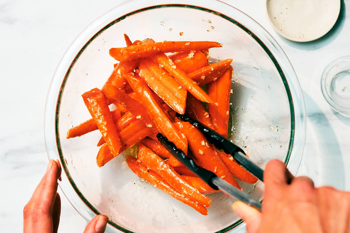 Carrots being tossed with honey, butter, and garlic in a glass bowl.