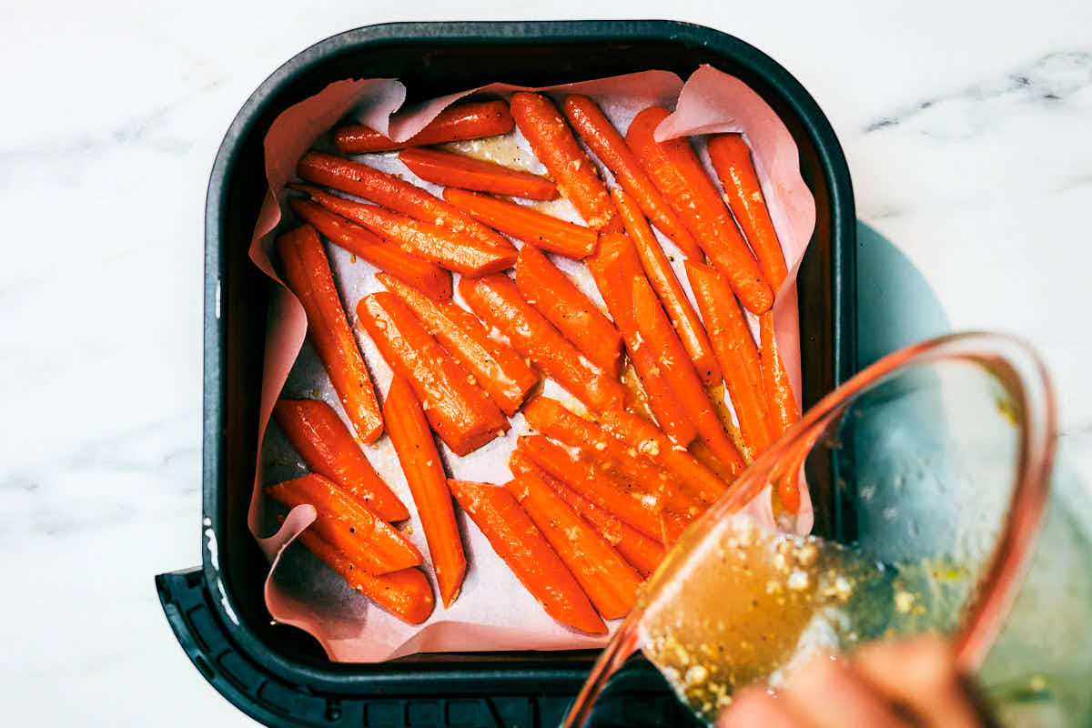 Carrots with honey, butter, and garlic in an air fryer basket before baking.