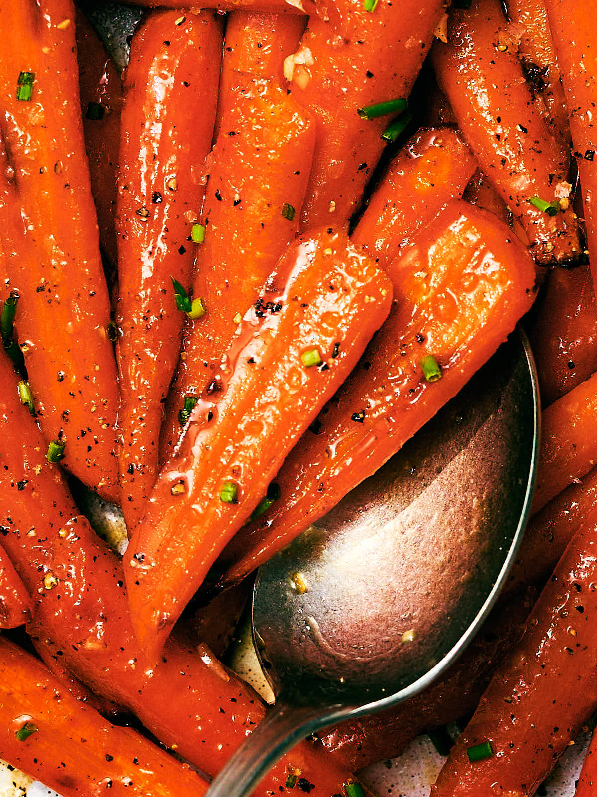 Honey Roasted Carrots with butter and chives being scooped with a spoon.