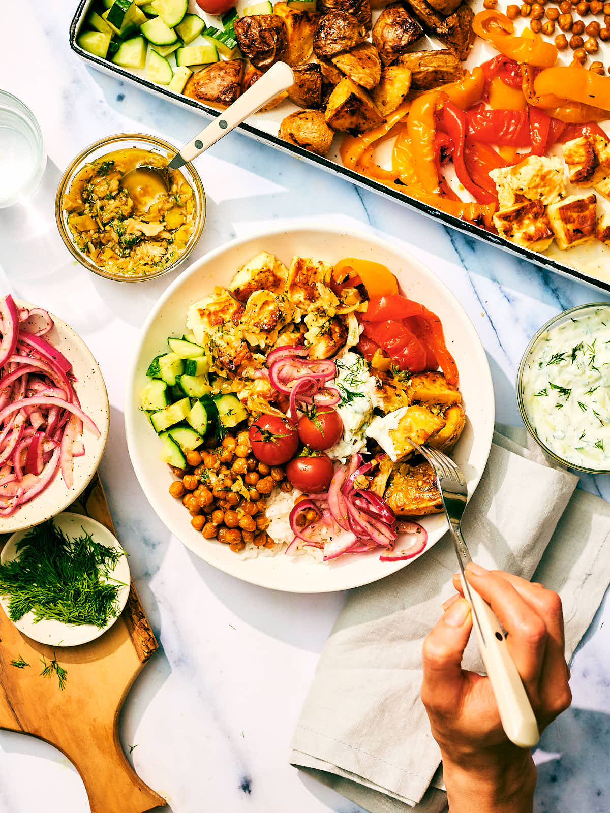 A sheet pan Greek Veggie Bowl with baked feta and tzatziki in a bowl with a fork.