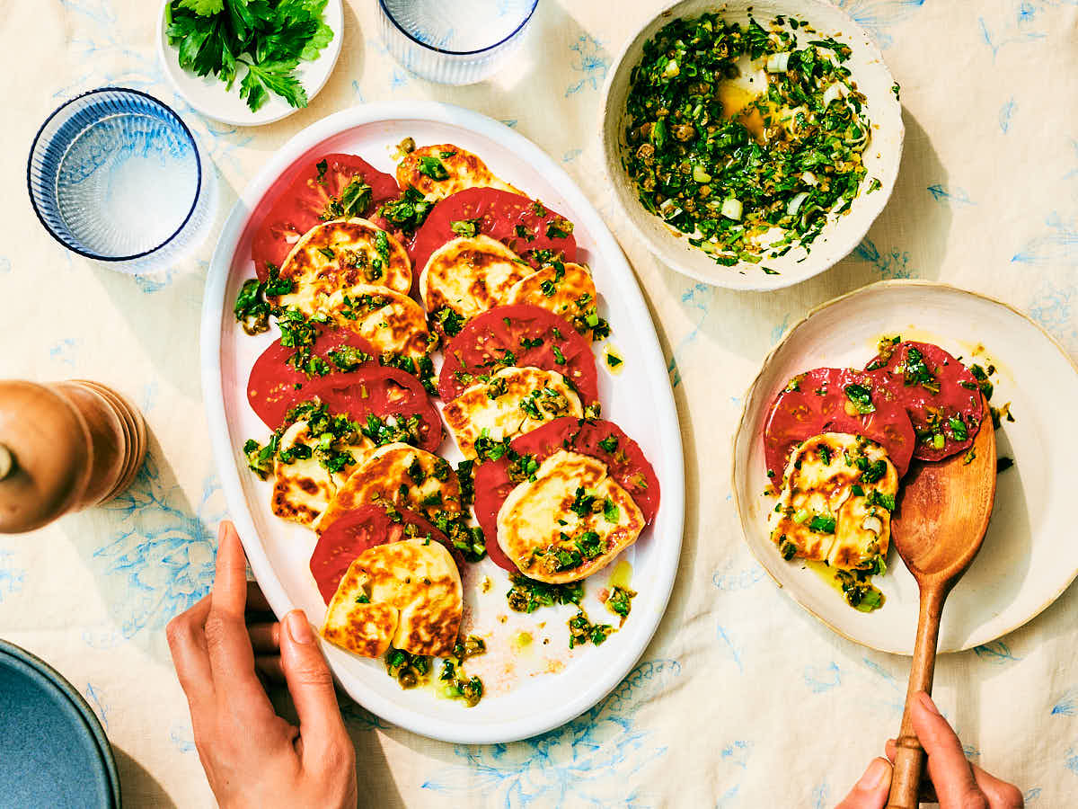 Seared Halloumi and Tomato Salad with herbs being spooned onto a plate.