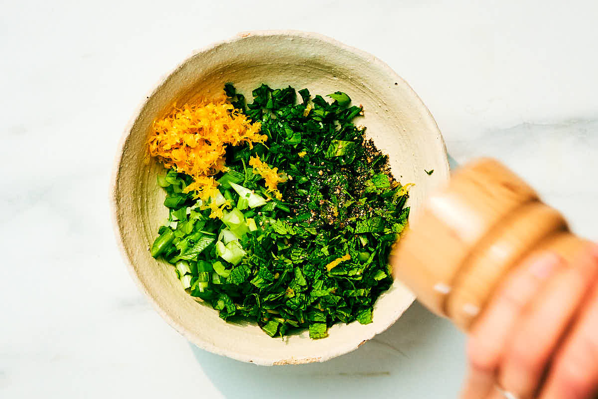 Fresh herbs, lemon, capers, and freshly cracked black pepper in a bowl.