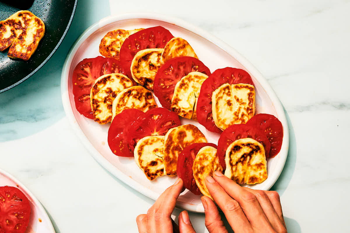 Seared halloumi cheese and slices of tomatoes being layered on serving platter.