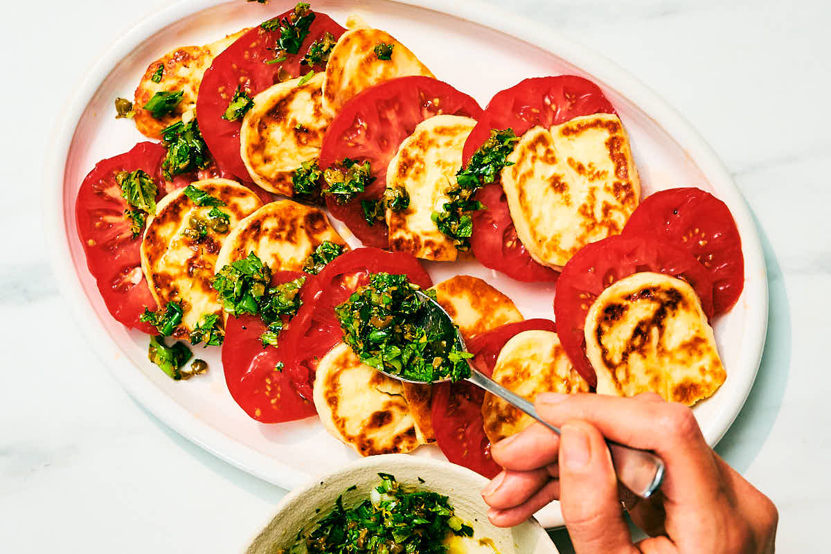 Fresh herb topping being scattered over a Halloumi and Tomato Salad.