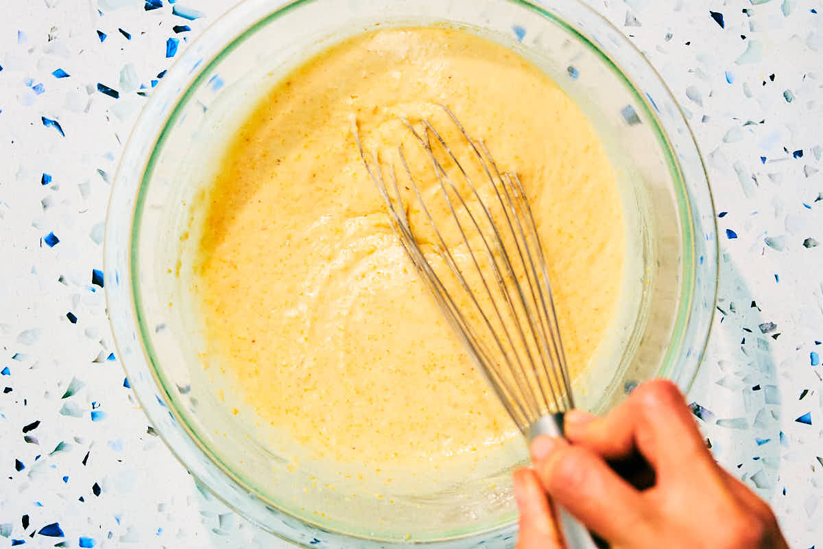 Mini cornbread muffin batter being whisked in a glass bowl.