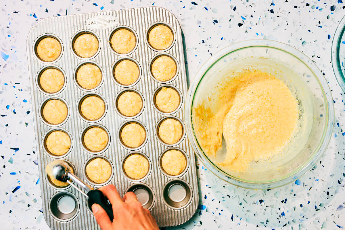 Cornbread batter being scooped into mini muffin tins.