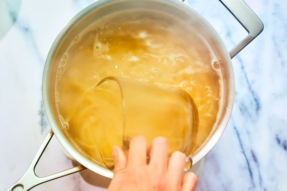 Pasta water being scooped out of a pot of boiling water.
