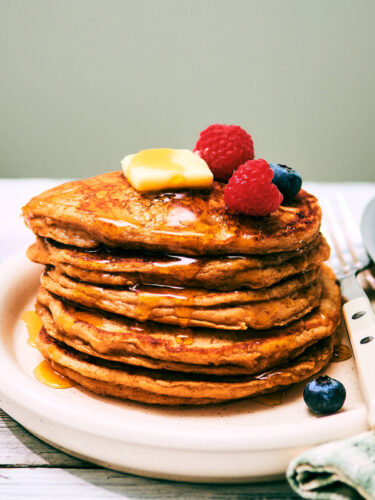 A stack of High Protein Cottage Cheese pancakes on a plate with berries.