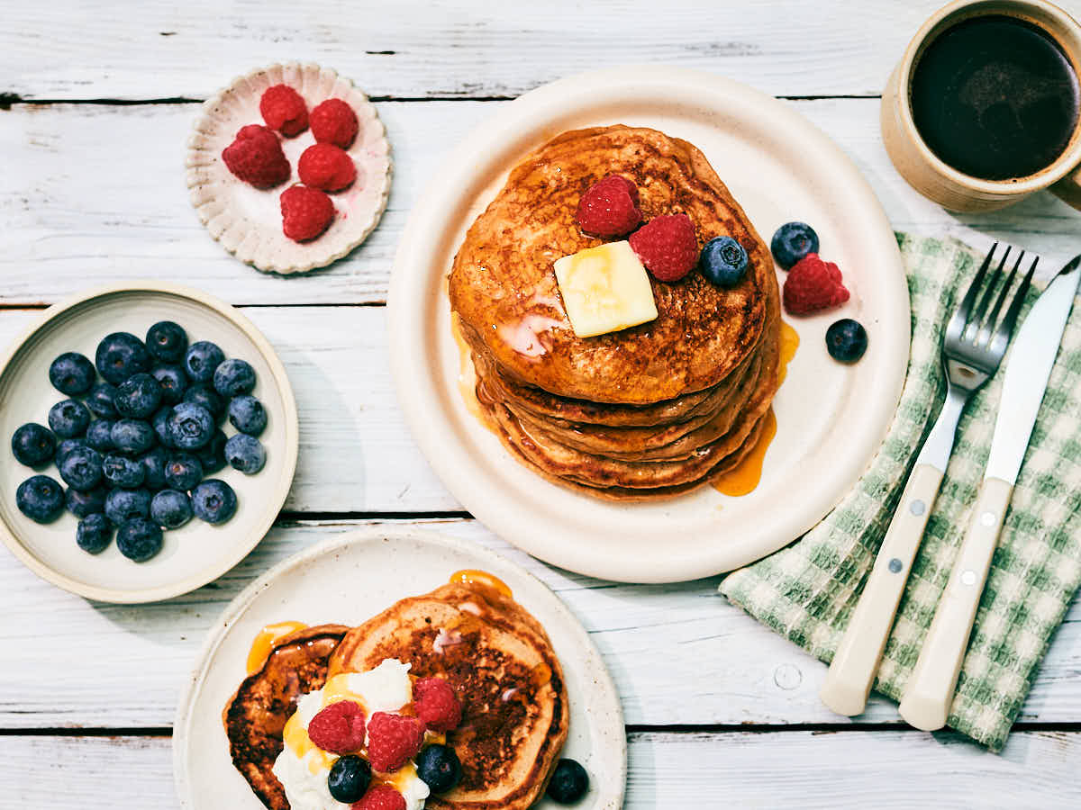 High protein Cottage Cheese Pancakes on plates topped with berries, butter, maple syrup on a breakfast table.