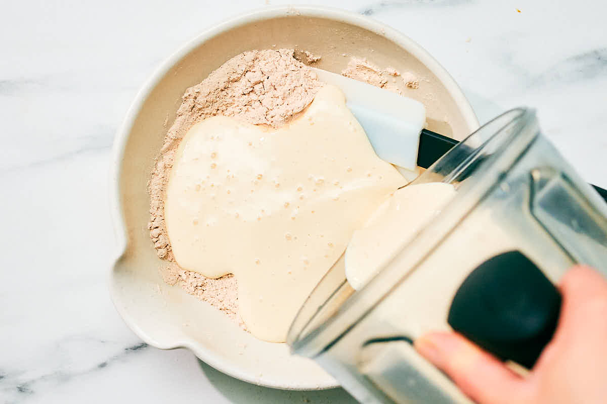 Adding wet ingredients from blender to dry ingredients in a bowl.