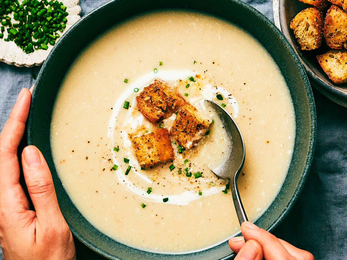 Slow Cooker Potato Leek Soup topped with croutons, being eaten out of a bowl with a spoon.