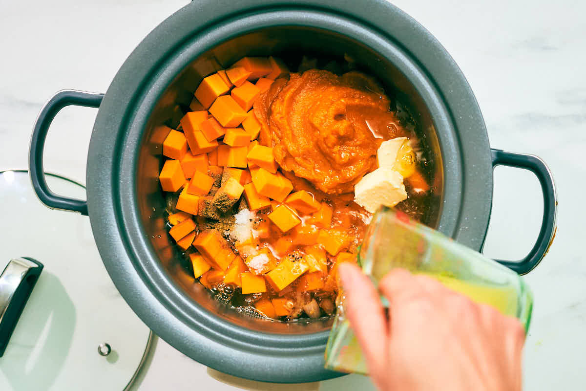 Combining ingredients in a slow cooker to make Pumpkin Soup.